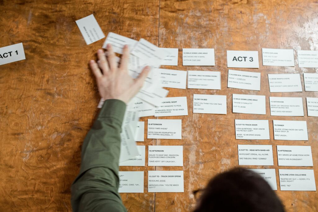 Leverage Post-Production A person arranging storyboard cards on a wooden table for a film script planning session.
